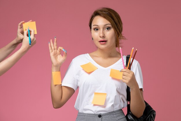 Widok z przodu młoda studentka w białej koszulce trzymając ołówki na różowym tle lekcje studia uniwersyteckie