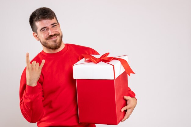 Widok z przodu młodego człowieka w czerwonej koszuli, posiadającego Boże Narodzenie obecny w pudełku na białej ścianie