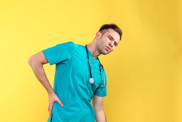 Widok z przodu młodego lekarza płci męskiej bóle pleców na żółtej ścianie