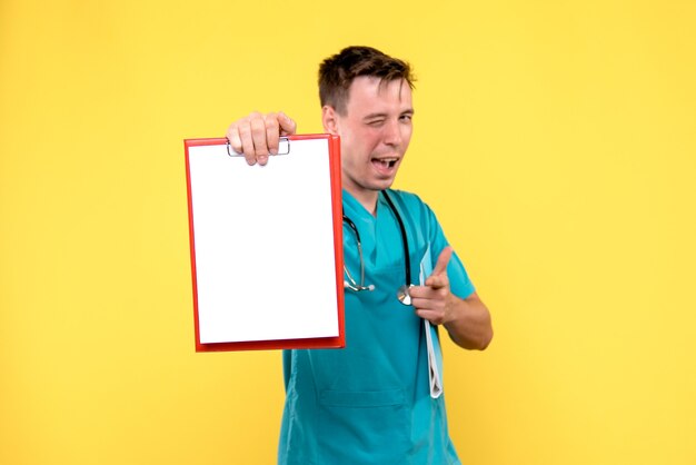 Widok z przodu młodego lekarza płci męskiej posiadających analizy na żółtej ścianie