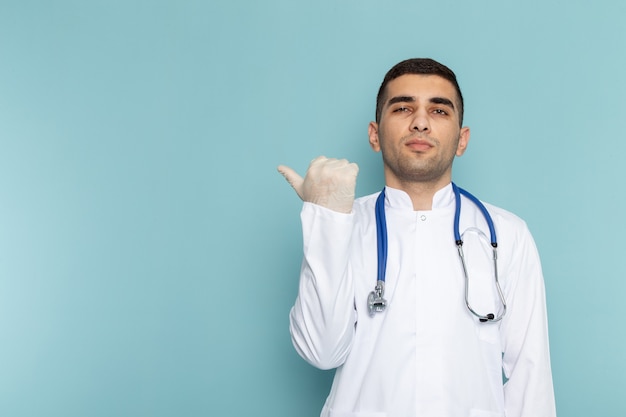 Widok z przodu młodego lekarza płci męskiej w białym garniturze z niebieskim stetoskopem pozowanie
