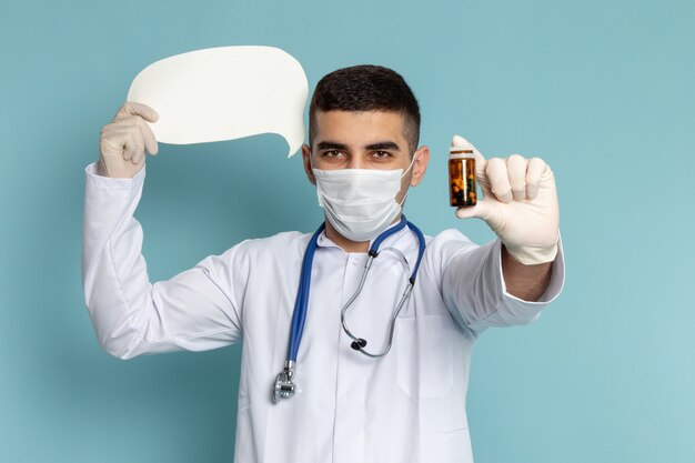 Widok z przodu młodego lekarza płci męskiej w białym garniturze z niebieskim stetoskopem, trzymając pigułki i biały znak