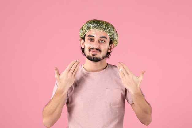 widok z przodu młodego mężczyzny nakładającego maskę na twarz na różowej ścianie