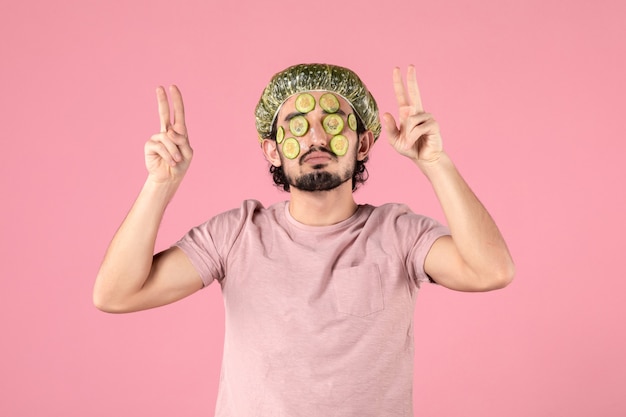 widok z przodu młodego mężczyzny nakładającego maskę ogórkową na twarz na różowej ścianie