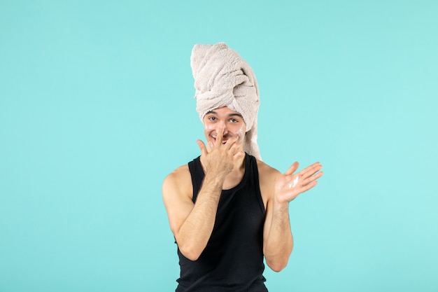 widok z przodu młodego mężczyzny po prysznicu nakładającego krem na twarz na niebieskiej ścianie