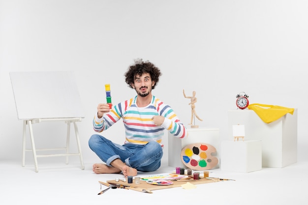 Widok z przodu młodego mężczyzny trzymającego farby do rysowania w małych puszkach na białej ścianie