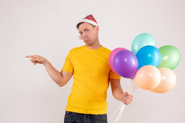 Widok z przodu młodego mężczyzny trzymającego kolorowe balony na białej ścianie