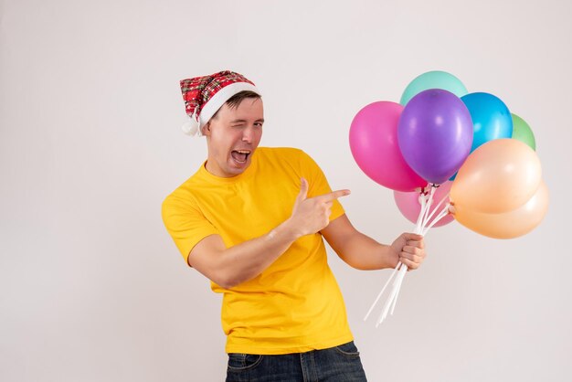 Widok z przodu młodego mężczyzny trzymającego kolorowe balony na białej ścianie