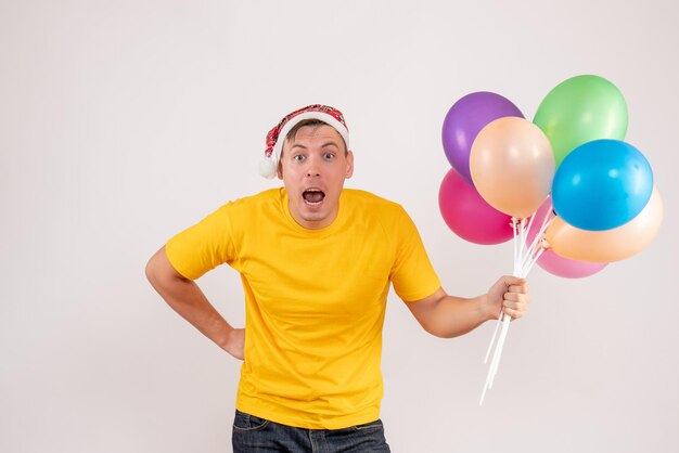 Widok z przodu młodego mężczyzny trzymającego kolorowe balony na białej ścianie
