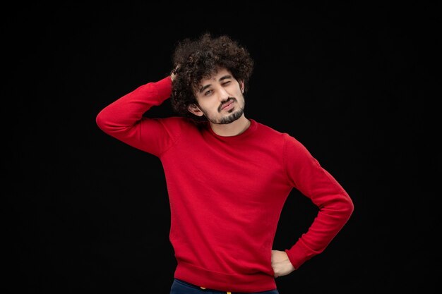 Widok z przodu młodego mężczyzny w czerwonym swetrze na czarnej ścianie
