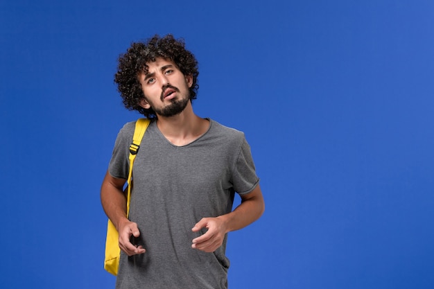 Widok z przodu młodego mężczyzny w szarej koszulce w żółtym plecaku na niebieskiej ścianie