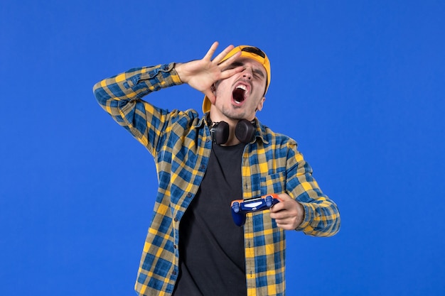 Bezpłatne zdjęcie widok z przodu młodego podekscytowanego mężczyzny z gamepadem grającym w grę wideo na niebieskiej ścianie