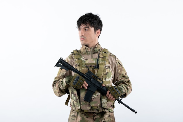 Widok z przodu młodego żołnierza w mundurze wojskowym z białą ścianą karabinu maszynowego