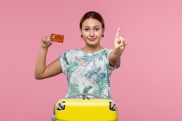 Widok z przodu młodej kobiety trzymającej brązową kartę bankową z uśmiechem na różowej ścianie