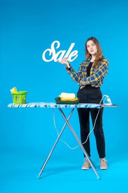 Widok z przodu młodej kobiety trzymającej ikonę sprzedaży i stojącej za deską do prasowania w pralni