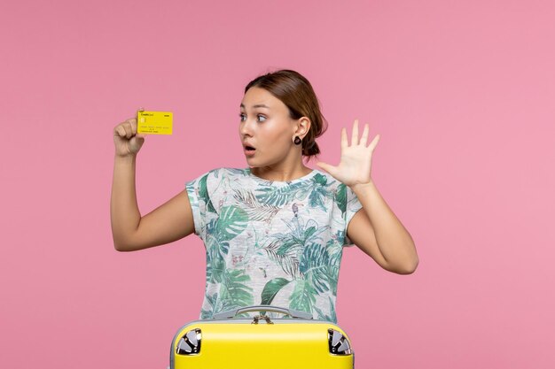 Widok z przodu młodej kobiety trzymającej żółtą kartę bankową na różowej ścianie