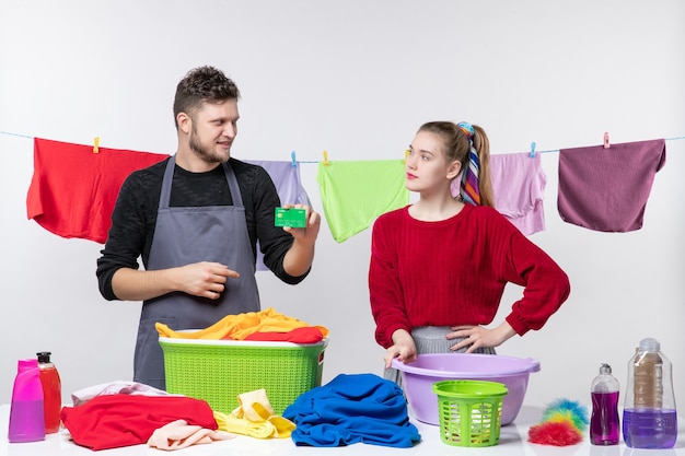 Widok z przodu młodej pary uśmiechniętego mężczyzny trzymającego kartę i kobiety kładącej rękę na talii na białej ścianie