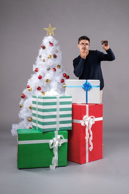 Widok z przodu młody człowiek posiadający kartę bankową na szarej podłodze nowy rok prezent świąteczny