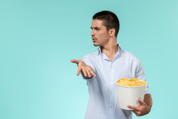 Widok z przodu młody człowiek trzymający kosz z ziemniakami, jedzenie i oglądanie filmu na niebieskiej ścianie samotne zdalne kino filmowe