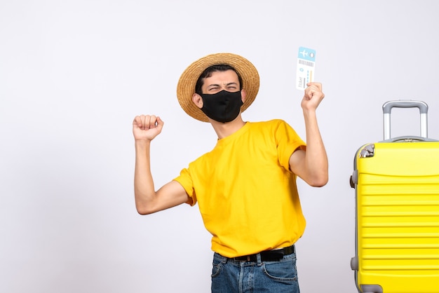 Widok Z Przodu Młody Człowiek W żółtej Koszulce Stojący W Pobliżu żółtej Walizki Trzymający Bilet Podróżny, Wyrażający Swoje Szczęście