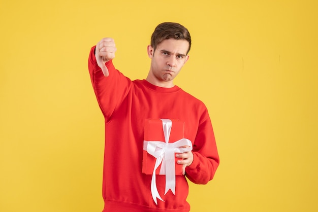 Widok z przodu młody człowiek z czerwonym swetrem robiąc kciuk w dół znak na żółtym tle