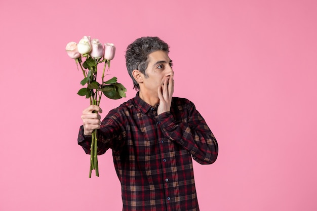 Widok z przodu młody człowiek z pięknymi różowymi różami na różowej ścianie