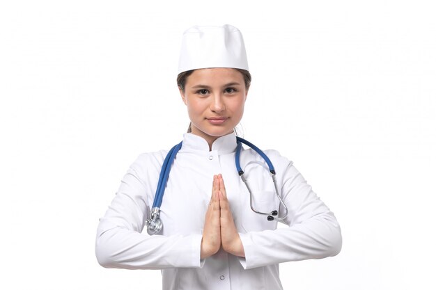 Widok z przodu młody lekarz kobiet w białym garniturze i białej czapce z uśmiechem niebieski stetoskop