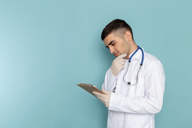Widok z przodu młody lekarz mężczyzna w białym garniturze z niebieskim stetoskopem trzymając notatnik z myśleniem wypowiedzi