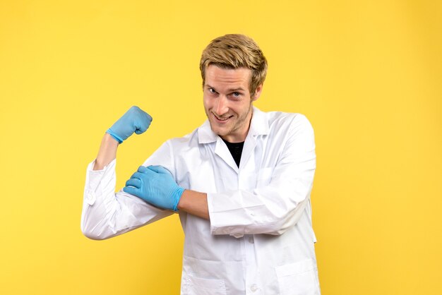 Widok z przodu młody lekarz płci męskiej uśmiechnięty na żółtym tle pandemia ludzkiego covid medic
