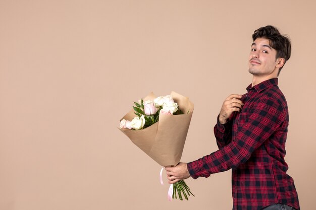 Widok z przodu młody mężczyzna dający piękne kwiaty na brązowej ścianie