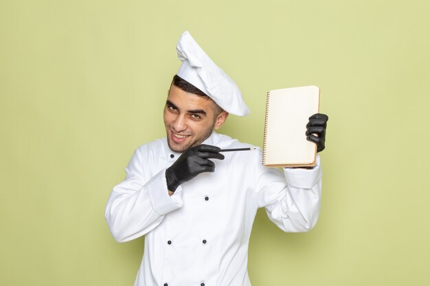 Widok z przodu młody mężczyzna kucharz w białym garniturze, trzymając notatnik i uśmiechając się na zielono
