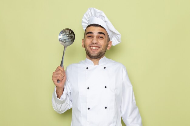 Widok z przodu młody mężczyzna kucharz w białym garniturze uśmiecha się i pozuje z łyżką na zielono