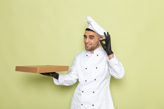 Widok z przodu młody mężczyzna kucharz w białym garniturze w czarnych skórzanych rękawiczkach, trzymając pudełko na zielono