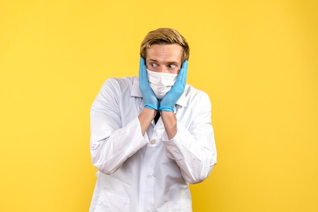 Widok z przodu młody mężczyzna lekarz na żółtym tle pandemiczny lekarz zdrowotny covid