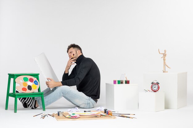 Widok z przodu młody mężczyzna próbuje narysować obraz z pomponem, myśląc na białej ścianie, kolorowy obraz, malowanie, malowanie, rysowanie artysty
