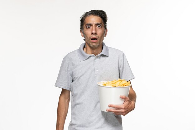 Widok z przodu młody mężczyzna trzyma chipsy ziemniaczane i ogląda film na białej powierzchni