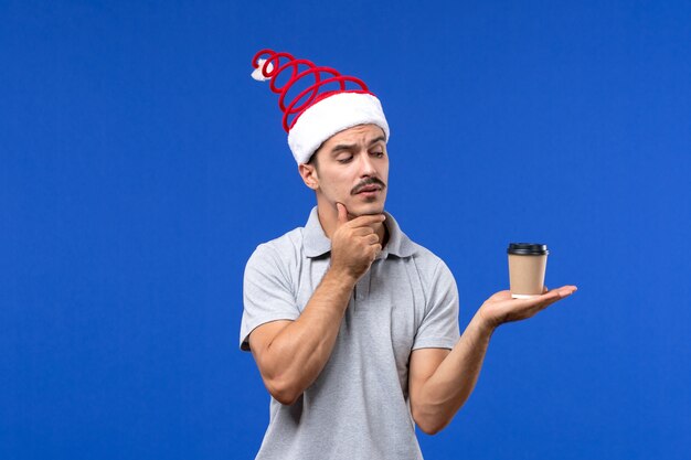 Widok z przodu młody mężczyzna trzyma plastikową filiżankę kawy na niebieskiej podłodze emocja mężczyzna nowy rok