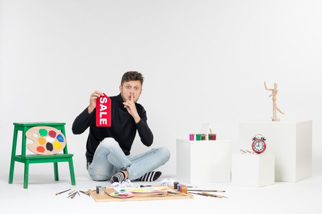 Widok z przodu młody mężczyzna trzyma sprzedaż pisanie na białej ścianie obraz kolor praca zakupy artysta farby