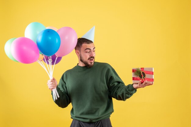 Widok z przodu młody mężczyzna trzymający kolorowe balony i obecny na żółtym tle