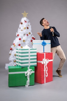 Widok z przodu młody mężczyzna trzymający mikrofon z prezentami na szarej podłodze świąteczne wakacje nowy rok
