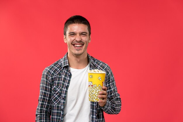 Widok z przodu młody mężczyzna trzymający popcorn i śmiejąc się na jasnoczerwonej ścianie męski film kino kino
