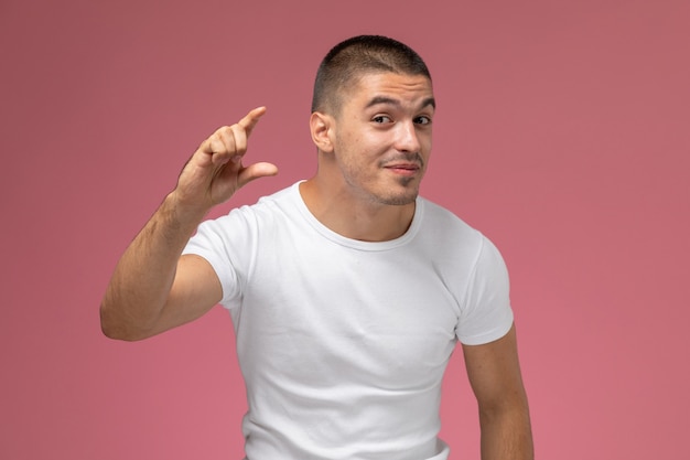 Widok z przodu młody mężczyzna w białej koszulce pokazujący rozmiar palcami na różowym tle