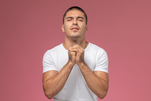 Bezpłatne zdjęcie widok z przodu młody mężczyzna w białej koszulce, pozowanie i modląc się na różowym tle