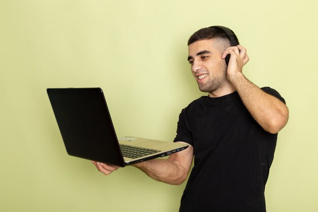 Widok Z Przodu Młody Mężczyzna W Czarnej Koszulce, Uśmiechając Się I Używając Laptopa Podczas Słuchania Muzyki Na Zielono