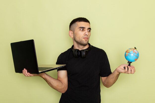 Widok z przodu młody mężczyzna w czarnej koszulce za pomocą laptopa trzymającego małą kulę ziemską na zielono