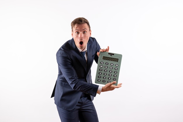 Widok z przodu młody mężczyzna w eleganckim klasycznym garniturze, trzymający ogromny kalkulator na białym biurku