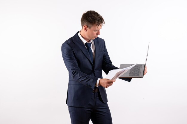 Widok z przodu młody mężczyzna w eleganckim klasycznym garniturze używający swojego laptopa na białym tle