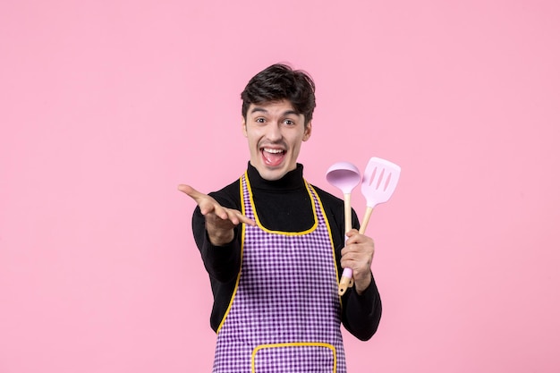 Widok z przodu młody mężczyzna w pelerynie trzymający łyżki na różowym tle zawód gotowanie posiłek poziomy kolor jedzenie jednolite ciasto kuchnia praca