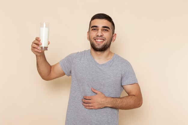 Widok z przodu młody mężczyzna w szarej koszulce pije mleko z uśmiechem na beżu