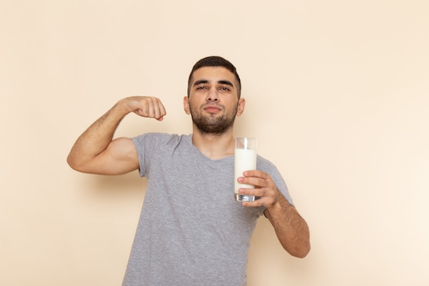 Widok z przodu młody mężczyzna w szarym t-shircie trzymający szklankę mleka na beżu